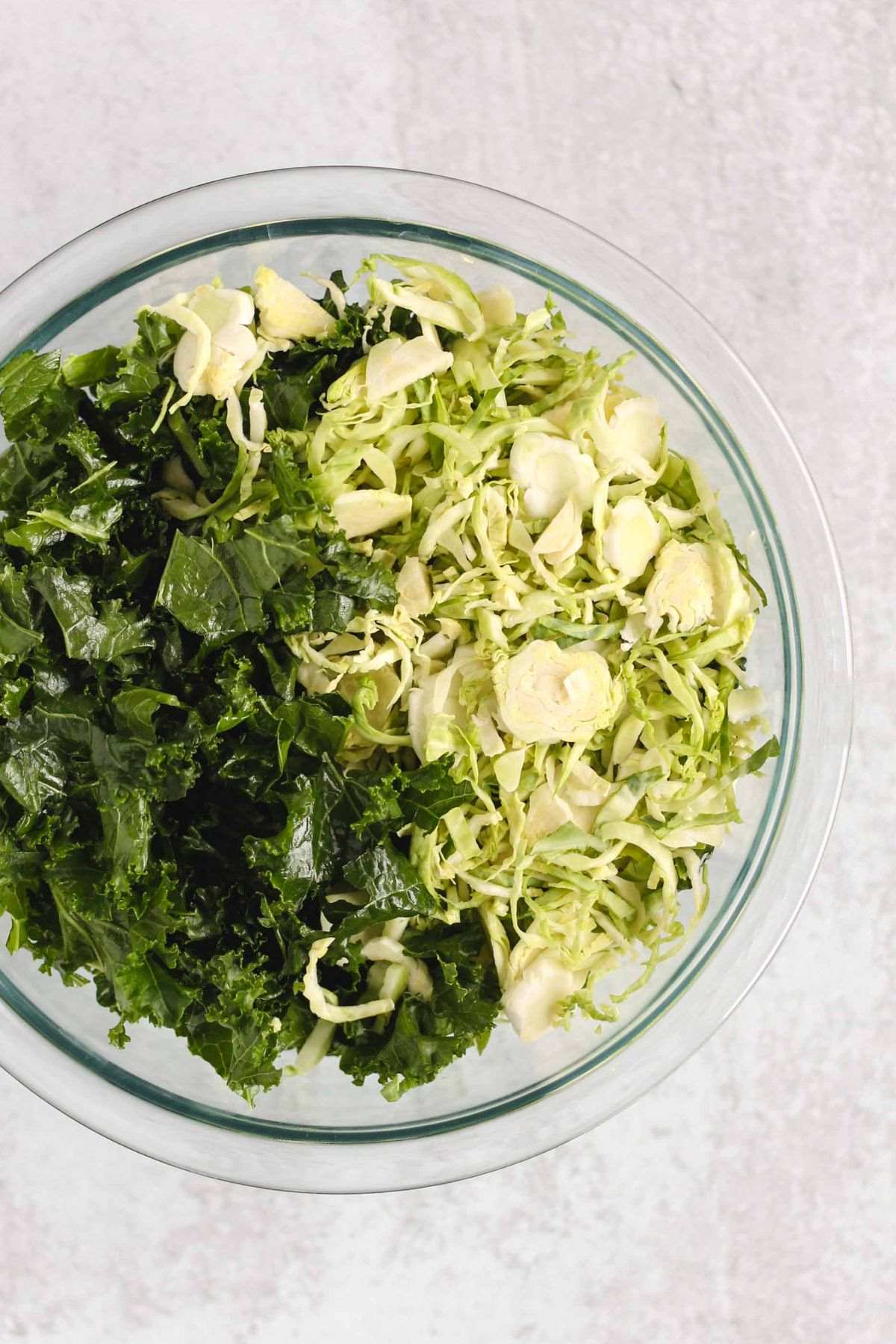 Shaved Brussels sprouts and kale leaves in a glass mixing bowl.