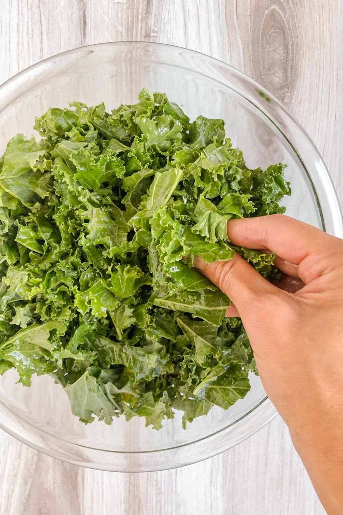 Hand massaging kale leaves in a glass mixing bowl.