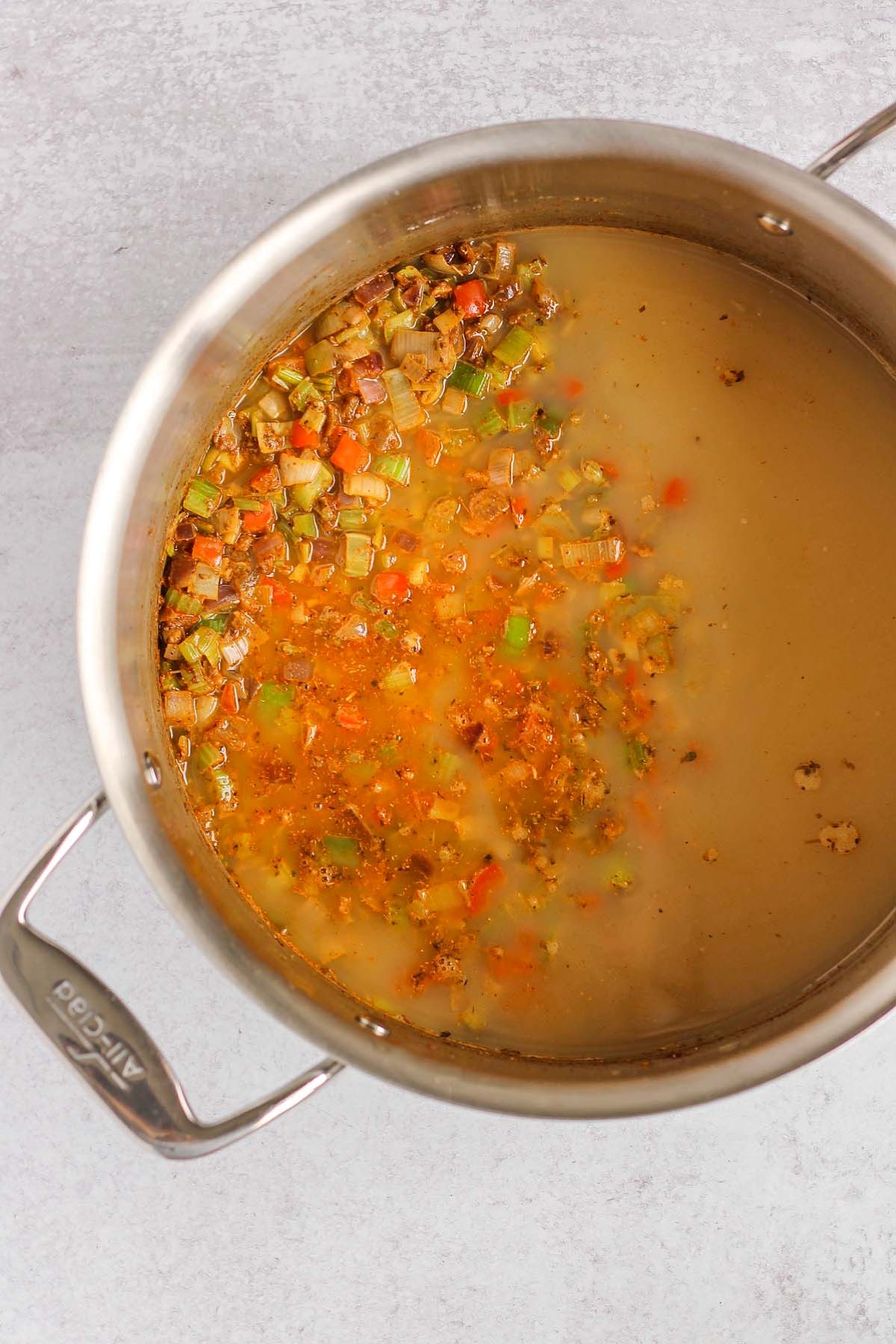 Sauteed veggies and spices plus added broth in a stainless steel pot.