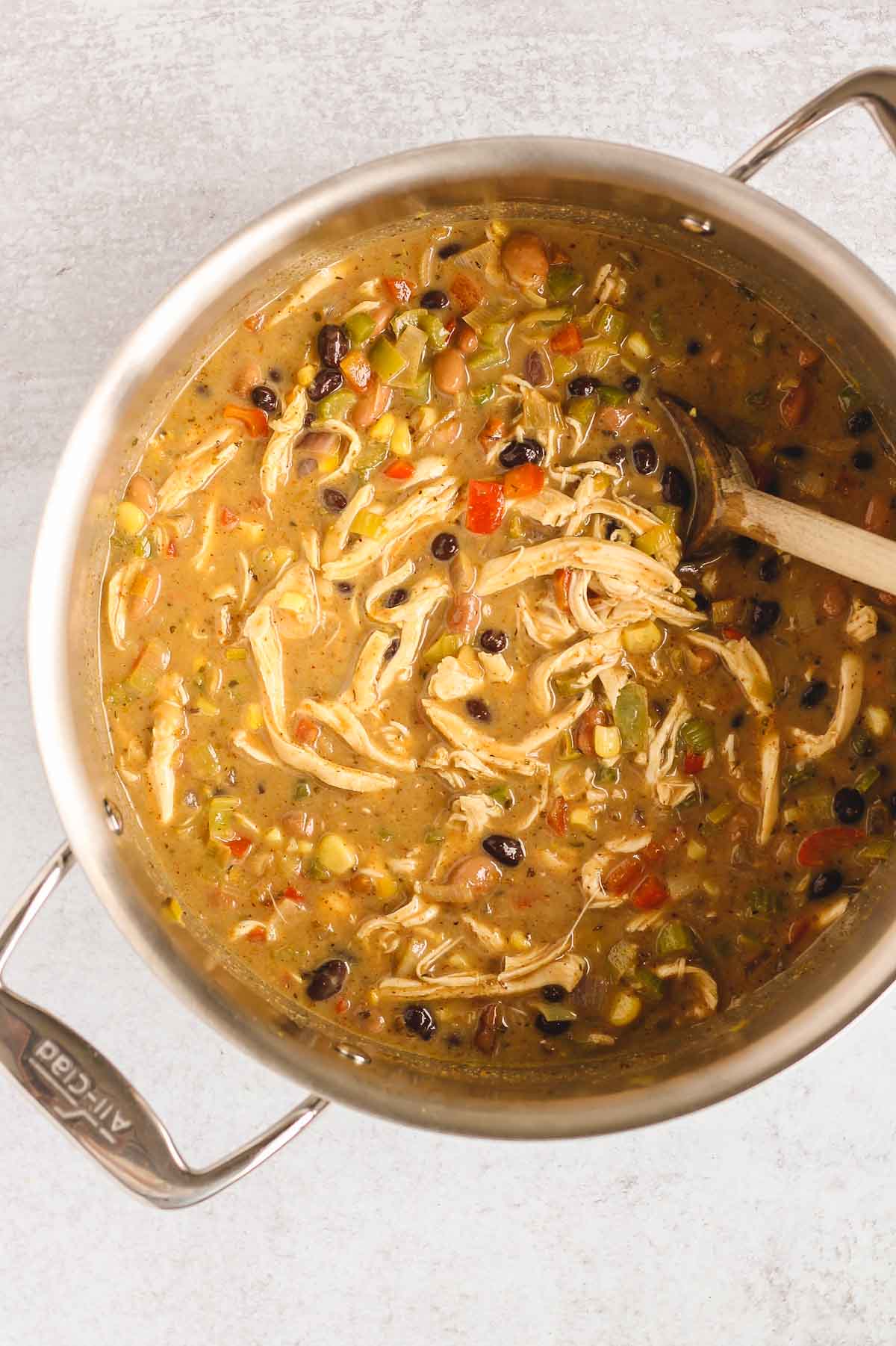 Wooden spoon stirring fully made southwest chicken chili in a stainless steel pot.