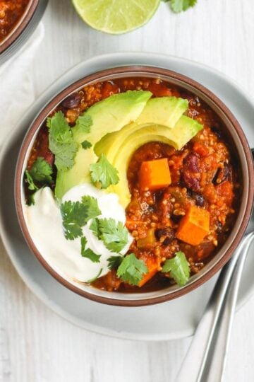 Vegetarian sweet potato topped with avocado, cilantro, and sour cream in a dark bowl sitting on a white plate.