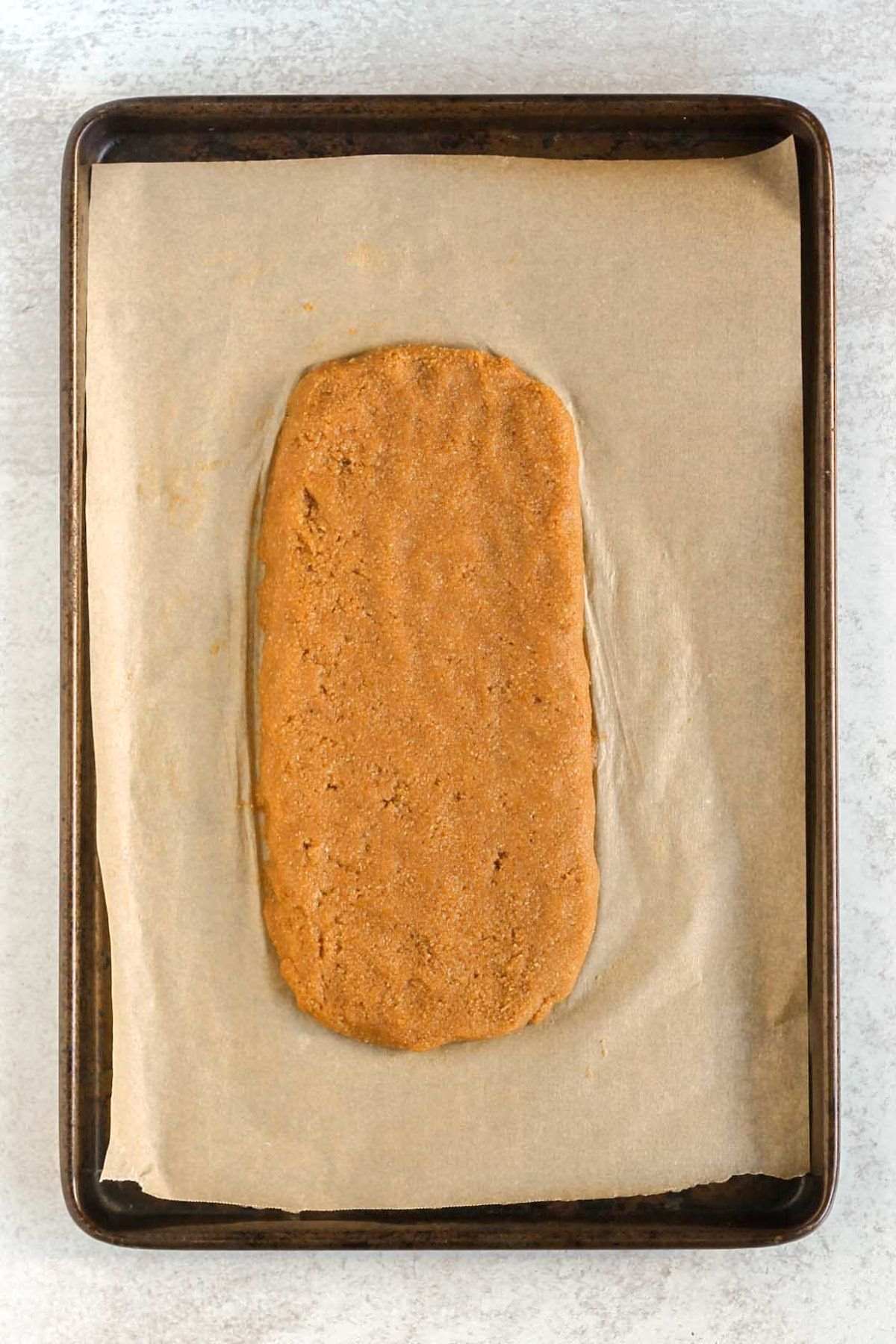 Almond flour biscotti dough shape into a log on a parchment paper lined baking sheet.