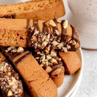 Biscotti drizzled with chocolate and almond pieces stacked on a plate.