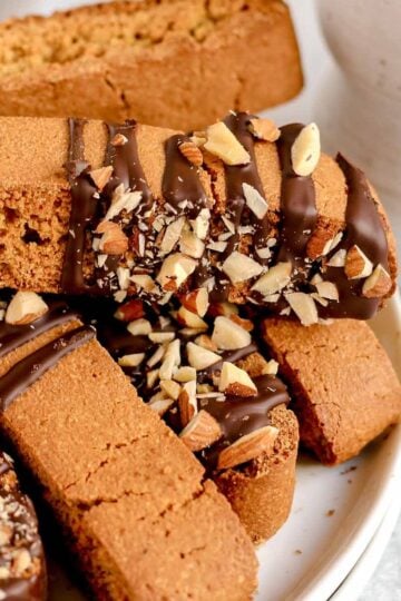 Biscotti drizzled with chocolate and almond pieces stacked on a plate.