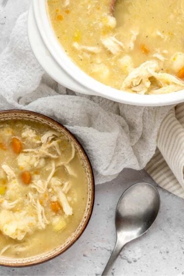 A bowl and larger soup crock next to each other filled with creamy chicken and cauliflower soup.
