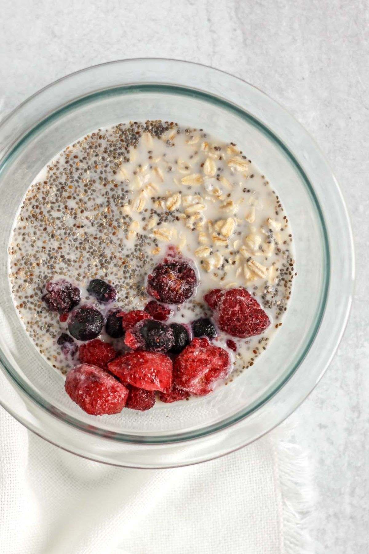 Mixing bowl with oats, milk, chia seeds, and frozen mixed berries.