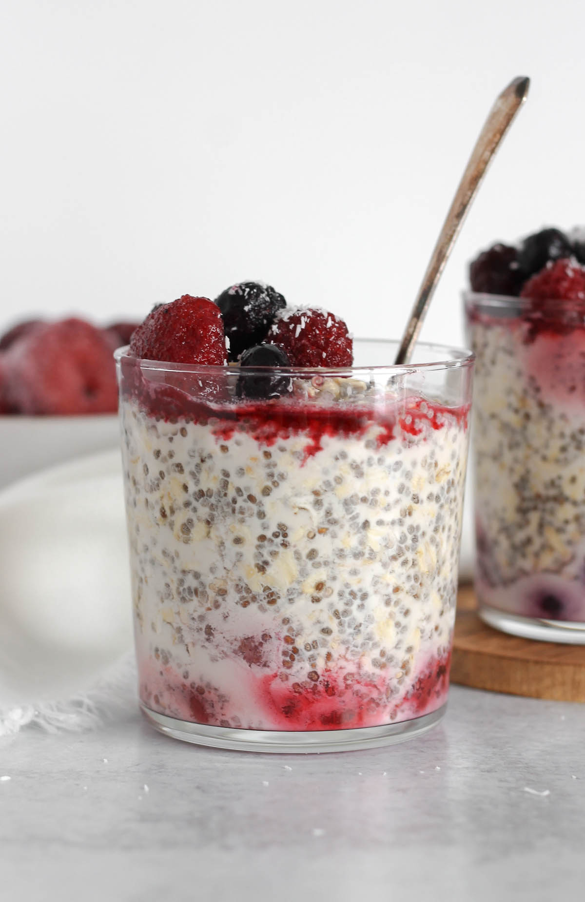 Glass cup filled with overnight oats topped with thawed frozen fruit with a vintage spoon in the glass.