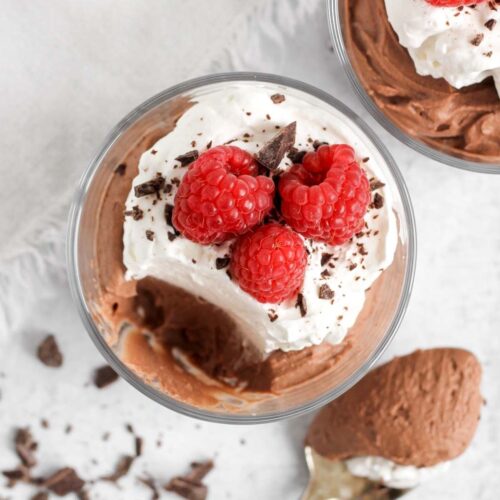 Chocolate mousse topped with whipped cream and raspberries in a small serving dish with a spoonful taken from the dish.