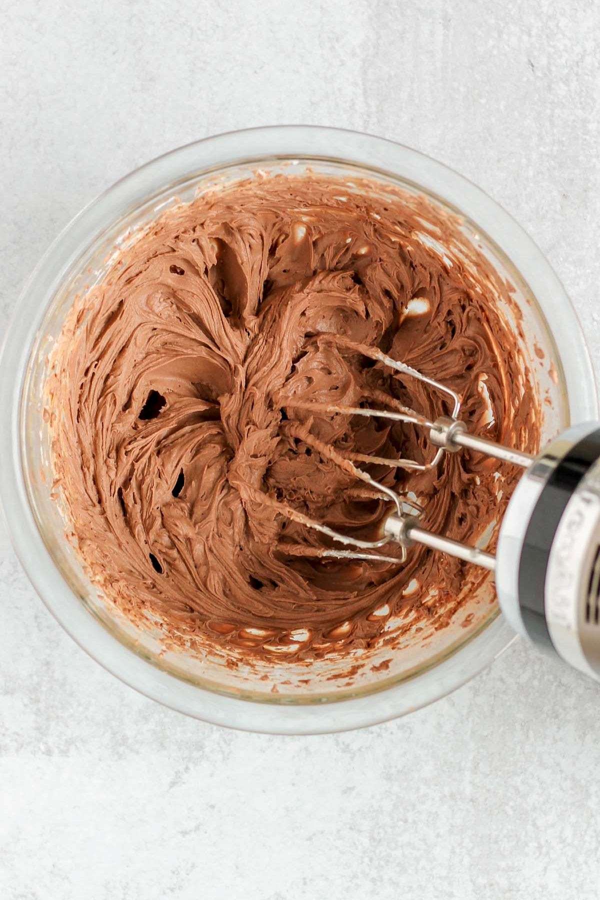 Vegan chocolate mousse whipped in a mixing bowl with a hand-held blender.
