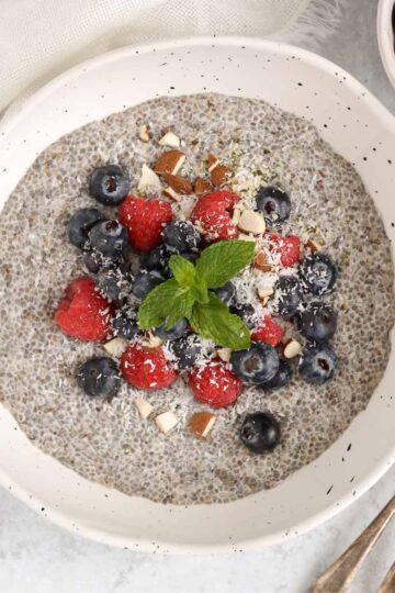 Chia bowl topped with fresh blueberries, raspberries, and chopped almonds with two vintage spoons in the bowl.