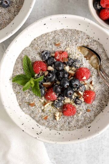 Chia seed breakfast bowl topped with fresh blueberries, raspberries, and chopped almonds with two vintage spoons in the bowl.