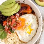 Breakfast burrito bowl topped with avocado and pico de gallo in a speckled bowl.