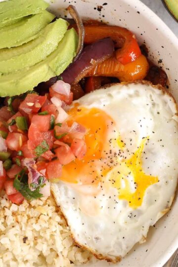 Breakfast burrito bowl topped with avocado and pico de gallo in a speckled bowl.