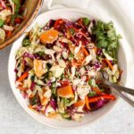 Asian cabbage salad sprinkled with sesame seeds and fresh cilantro in a small white bowl with two vintage forks.