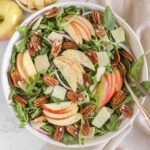 Arugula and apple salad with pecans, parmesan cheese, and red onion in a large salad bowl with vintage silverware.