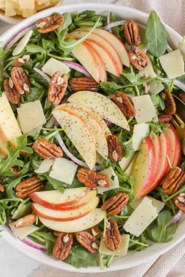 Arugula and apple salad with pecans, parmesan cheese, and red onion in a large salad bowl with vintage silverware.