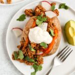 Chili stuffed sweet potato topped with sour cream, cilantro, and radishes with avocado on the side.