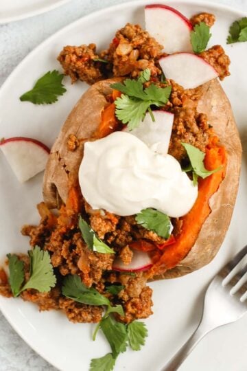 Chili stuffed sweet potato topped with sour cream, cilantro, and radishes with avocado on the side.