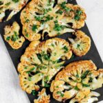 Roasted cauliflower steaks sprinkled with fresh parsley on a baking sheet.