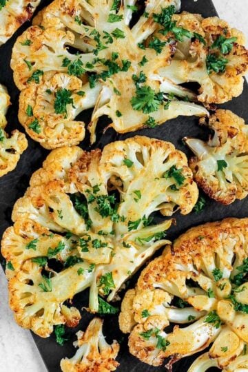 Roasted cauliflower steaks sprinkled with fresh parsley on a baking sheet.
