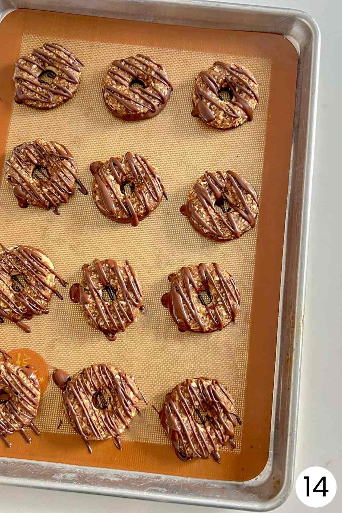 Samoa cookies freshly drizzled with melted chocolate on a baking sheet.