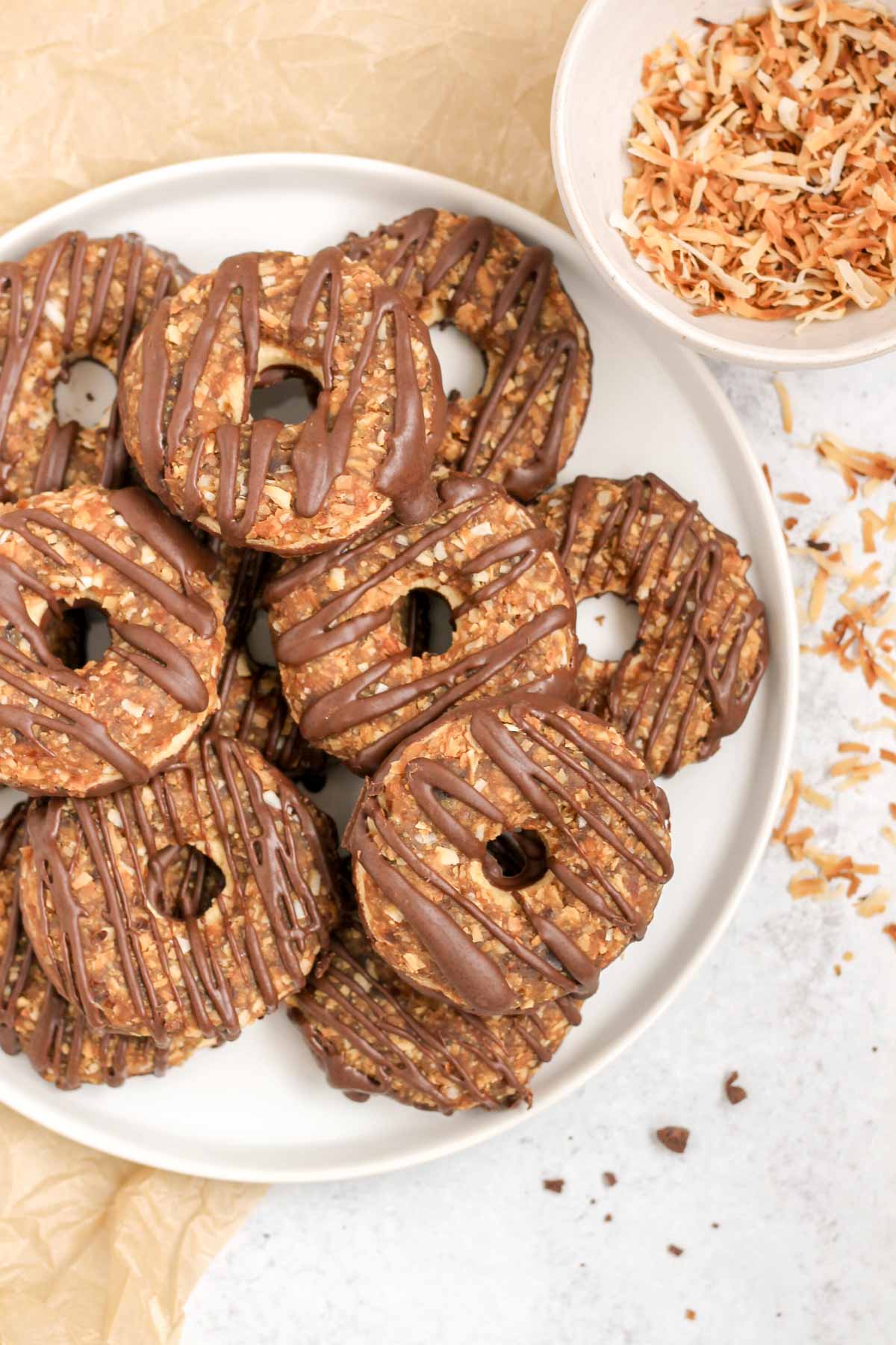 Homemade Samoa cookies on a round plate with a bowl of toasted coconut on the side.
