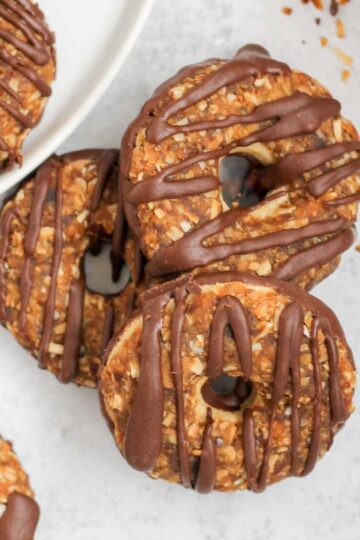 Three Samoa cookies slightly stacked on a gray surface with additional cookies around the side.