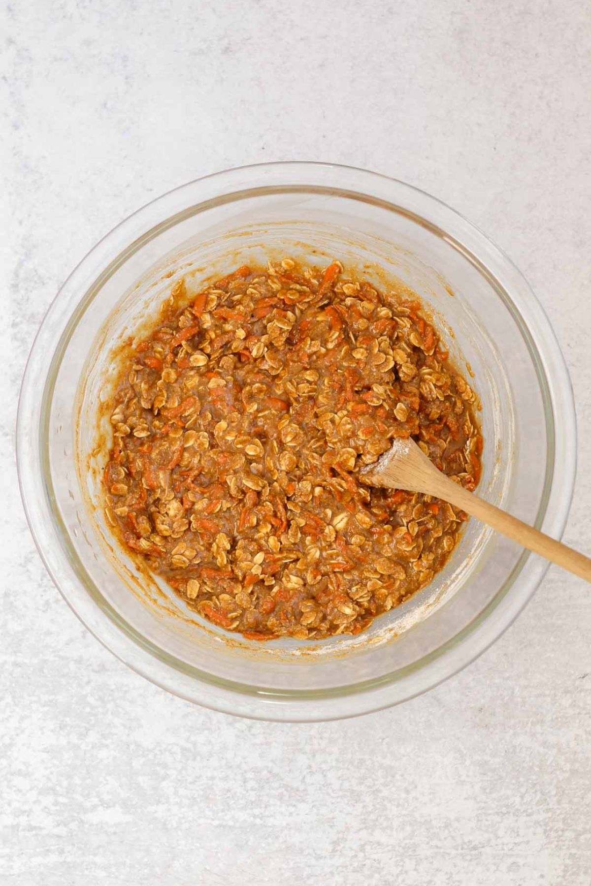 Carrot cake oatmeal cookie dough mixed in a glass mixing bowl with a wooden spoon.