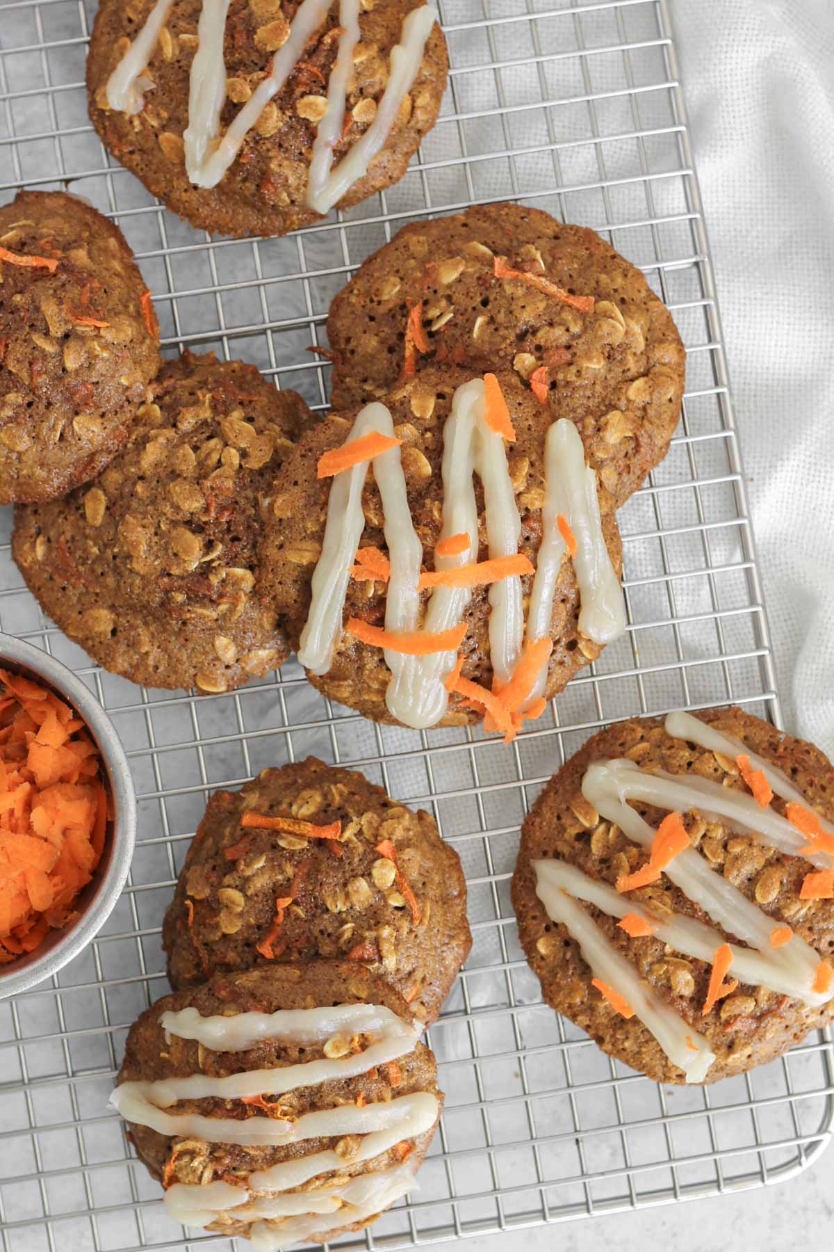 Carrot cake oatmeal cookies, some with a glaze on the top, on a rectangular wire cooling rack.