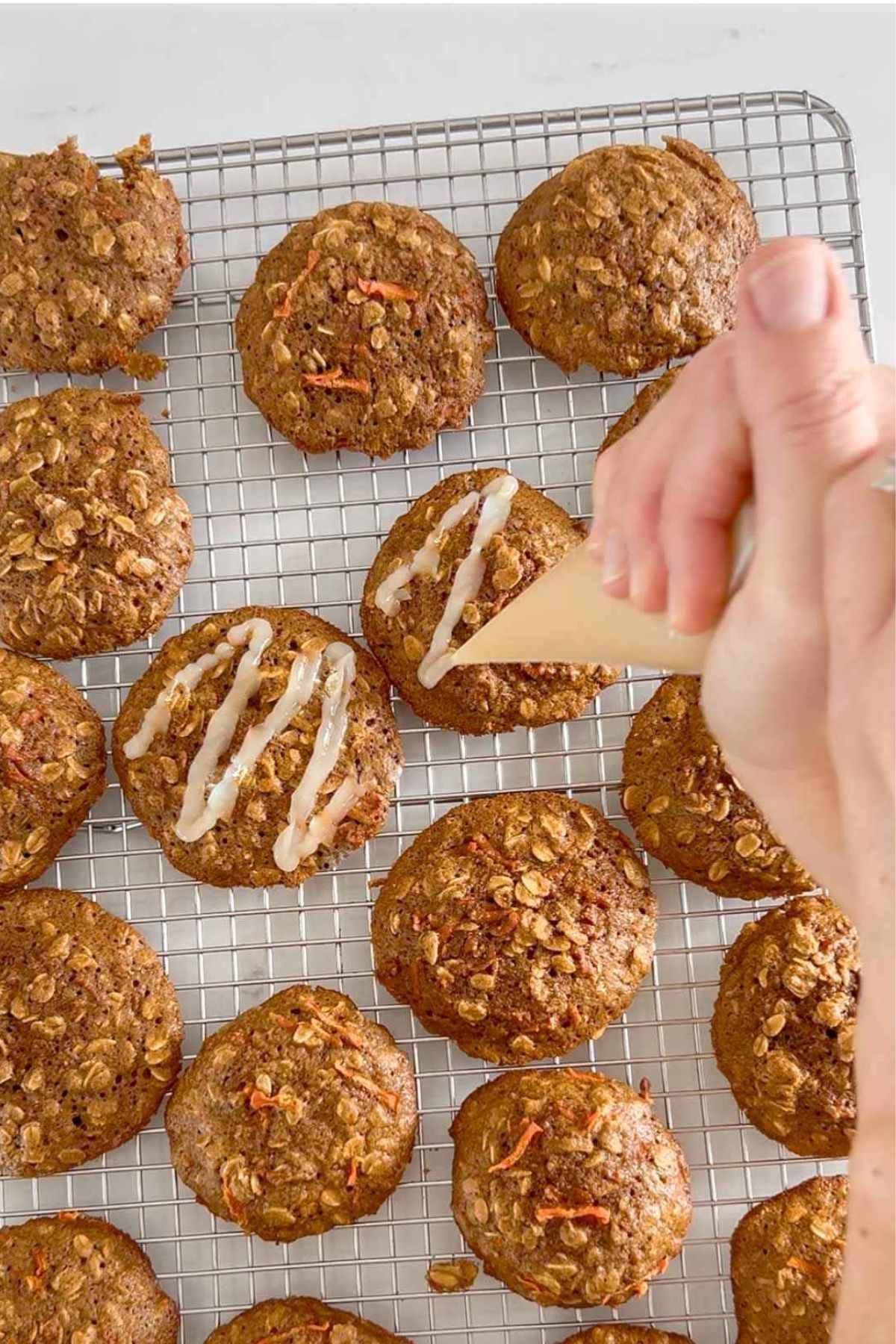 Carrot cake oatmeal cookies being glazed with glazed from a piping bag.