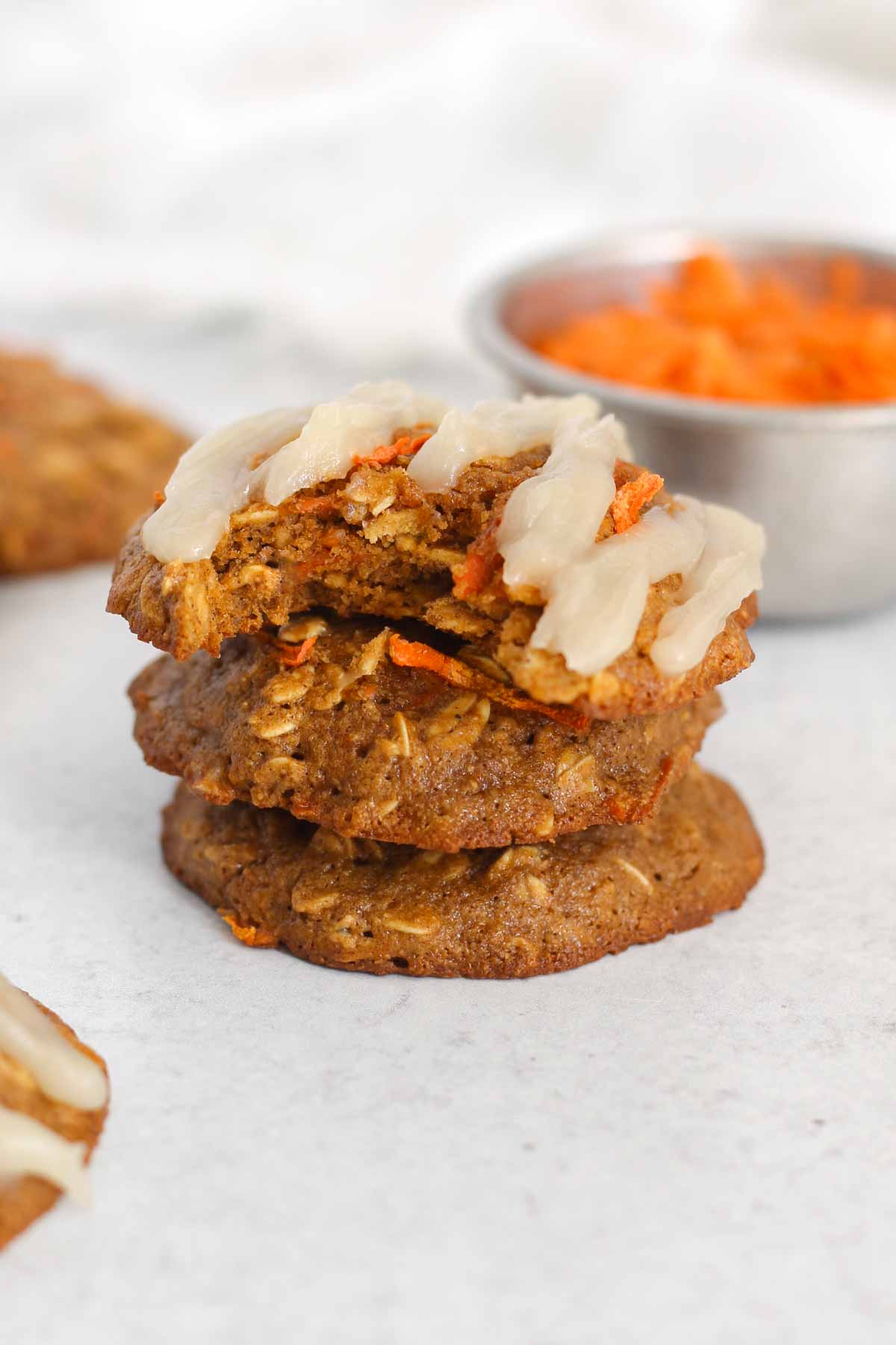 Oatmeal carrot cake cookies stacked 3 high with a bit taken from the top one to show texture.