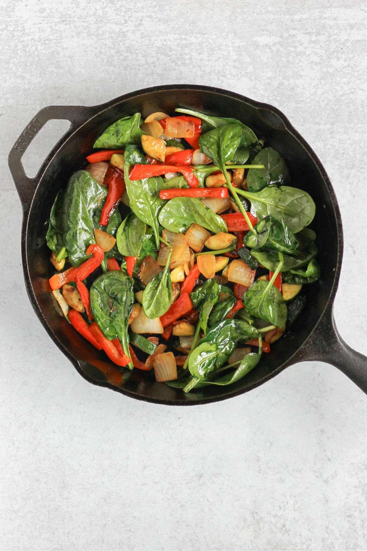 Sauteed veggies with spinach in a cast iron skillet.