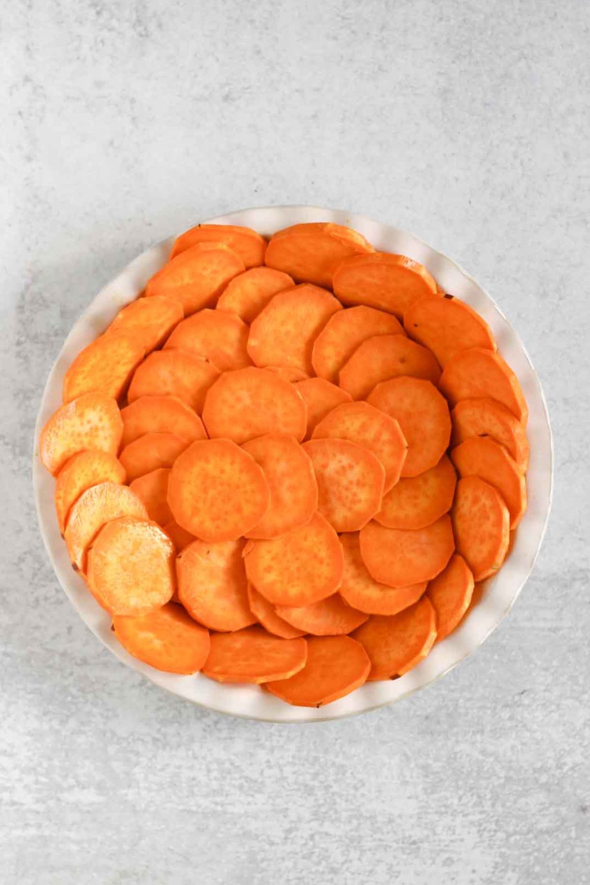 Raw sweet potato slices in a white pie plate.