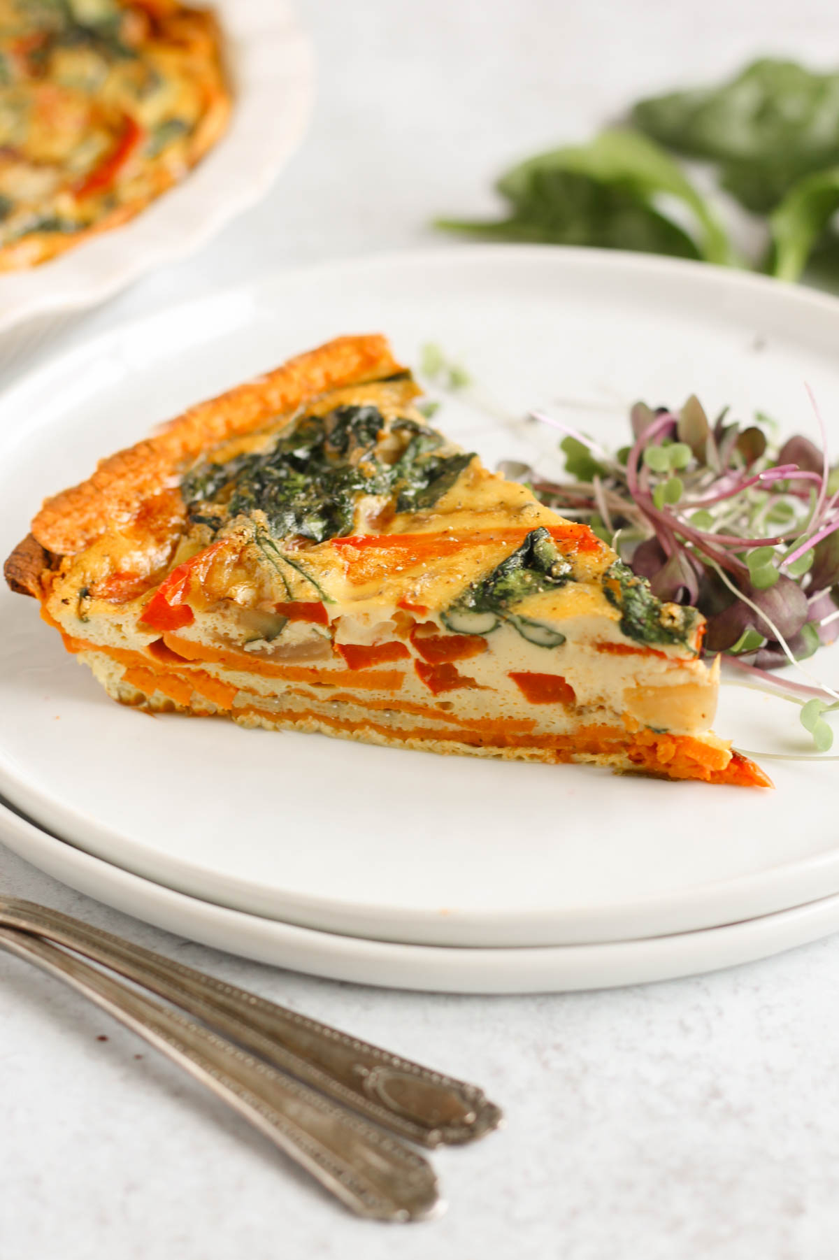 Slice of sweet potato crust quiche on two stacked white plates with vintage forks near the plate.