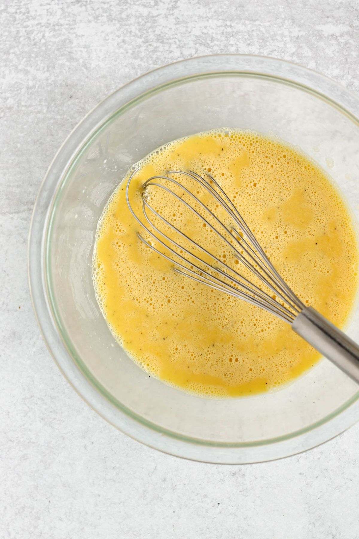 Whisked eggs in a glass mixing bowl with a wire whisk.