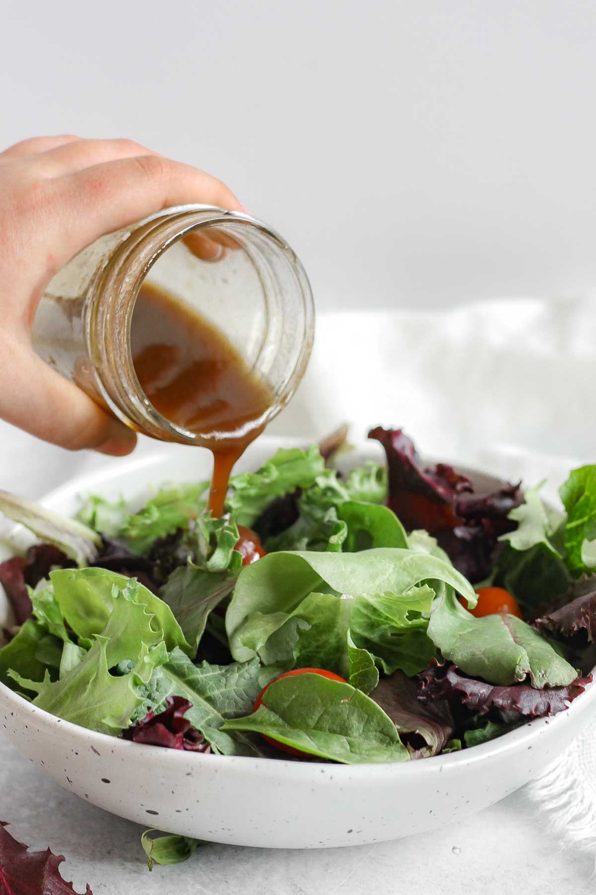 Balsamic vinaigrette being poured over a bowl of mixed greens.