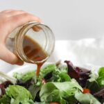 Balsamic vinaigrette being poured from a mason jar onto a bed of mixed greens.