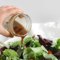 Balsamic vinaigrette being poured from a mason jar onto a bed of mixed greens.