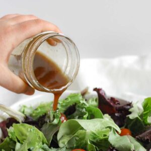 Balsamic vinaigrette being poured from a mason jar onto a bed of mixed greens.