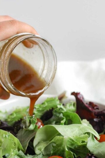 Balsamic vinaigrette being poured from a mason jar onto a bed of mixed greens.