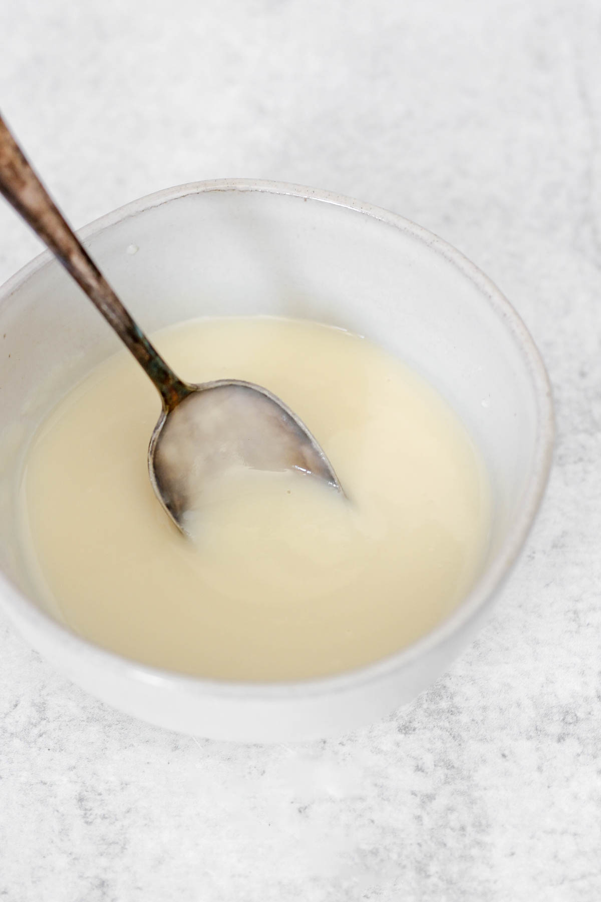 Coconut butter glaze in a bowl with a small spoon scooping up some glaze.