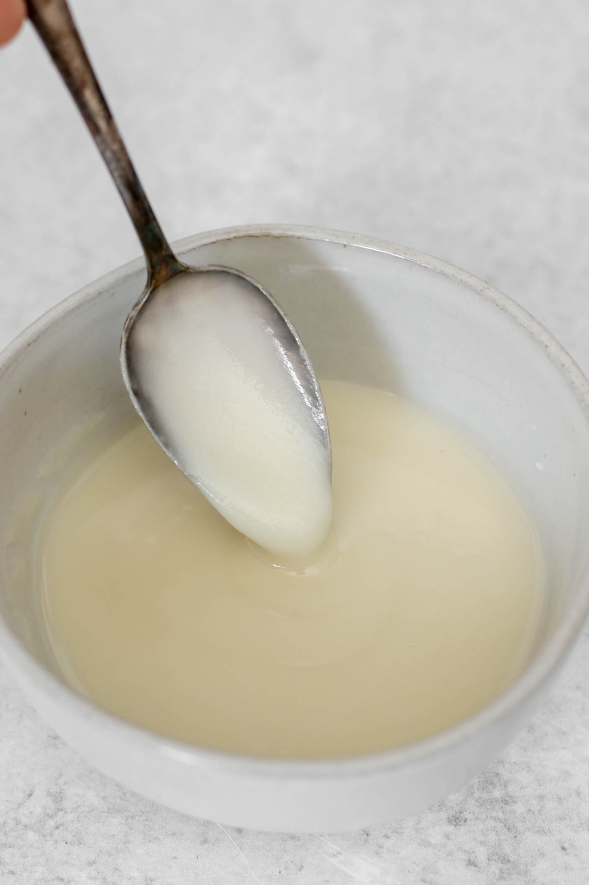 Coconut butter glaze dripping from a spoon in a small ceramic bowl.