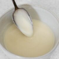 Coconut butter glaze dripping from a spoon in a small ceramic bowl.