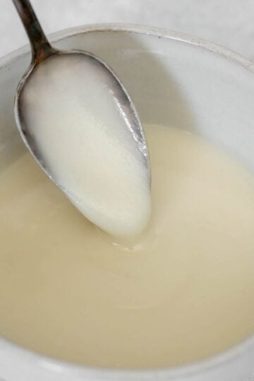 Coconut butter glaze dripping from a spoon in a small ceramic bowl.