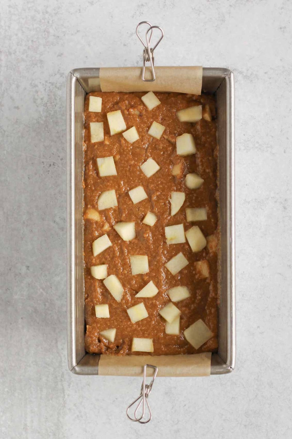 Loaf pan with apple bread batter and chopped apples sprinkled on top.
