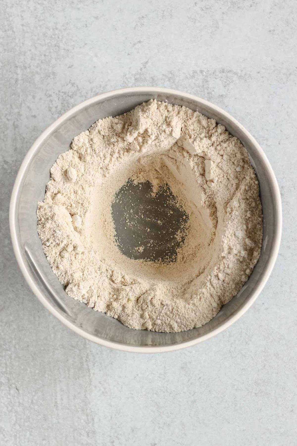 Dry ingredients needed for apple bread mixed together in a mixing bowl with a well in the center of the ingredients.