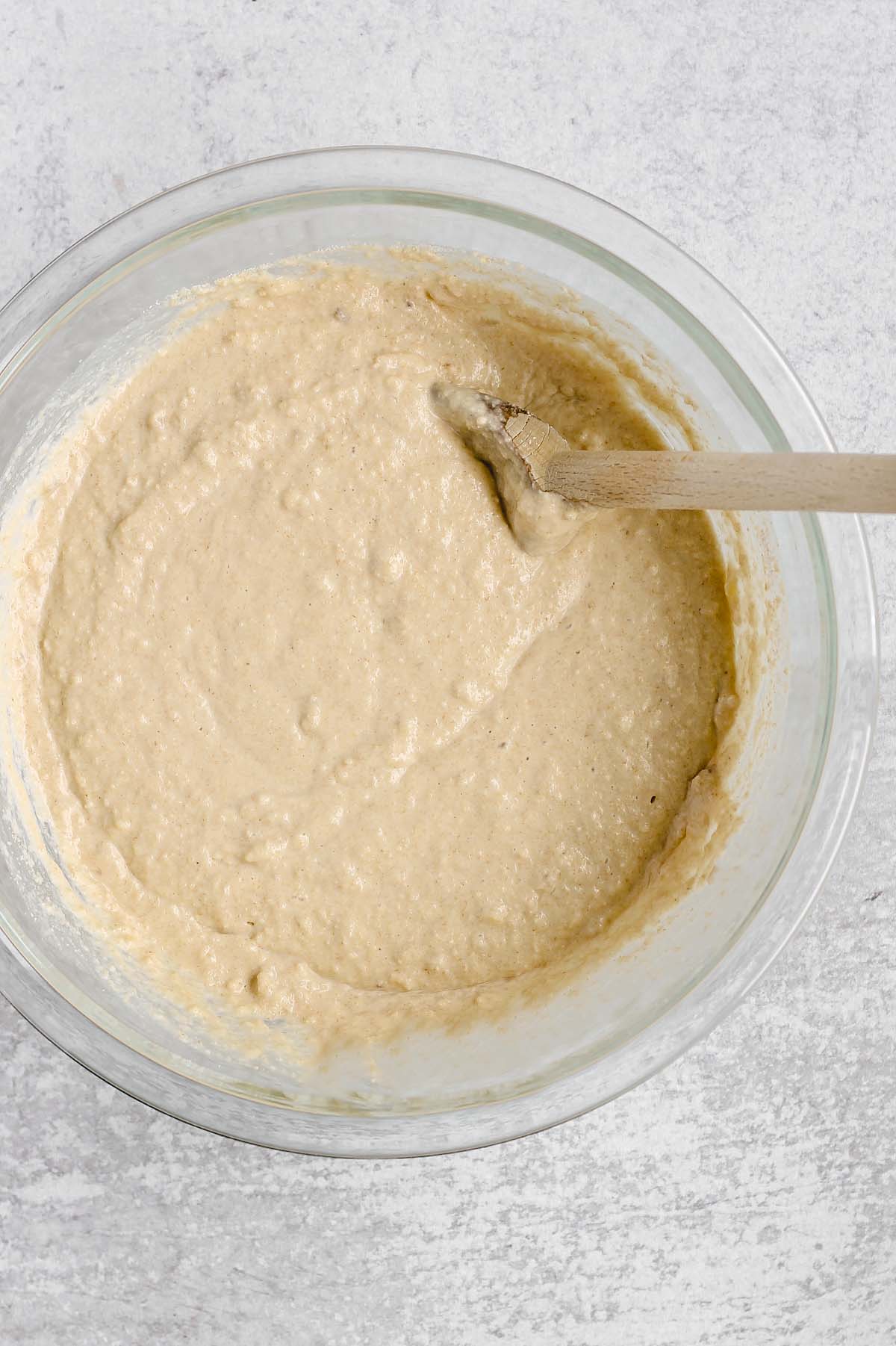 Gluten-free waffle batter in a glass mixing bowl with a wooden spoon.