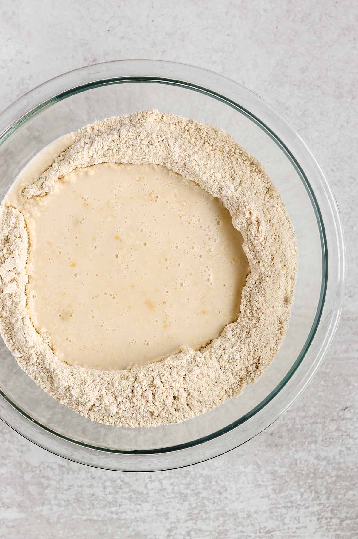 Dry ingredients and wet ingredients needed for gluten-free waffles in a glass mixing bowl.