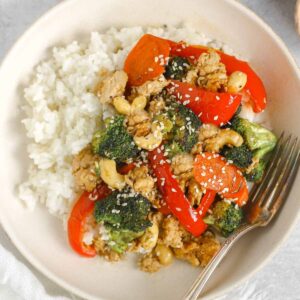 Ground chicken stir fry with veggies and a side of rice in a singe serve shallow bowl with a vintage fork.