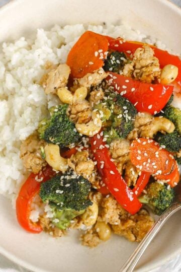 Ground chicken stir fry with veggies and a side of rice in a singe serve shallow bowl with a vintage fork.
